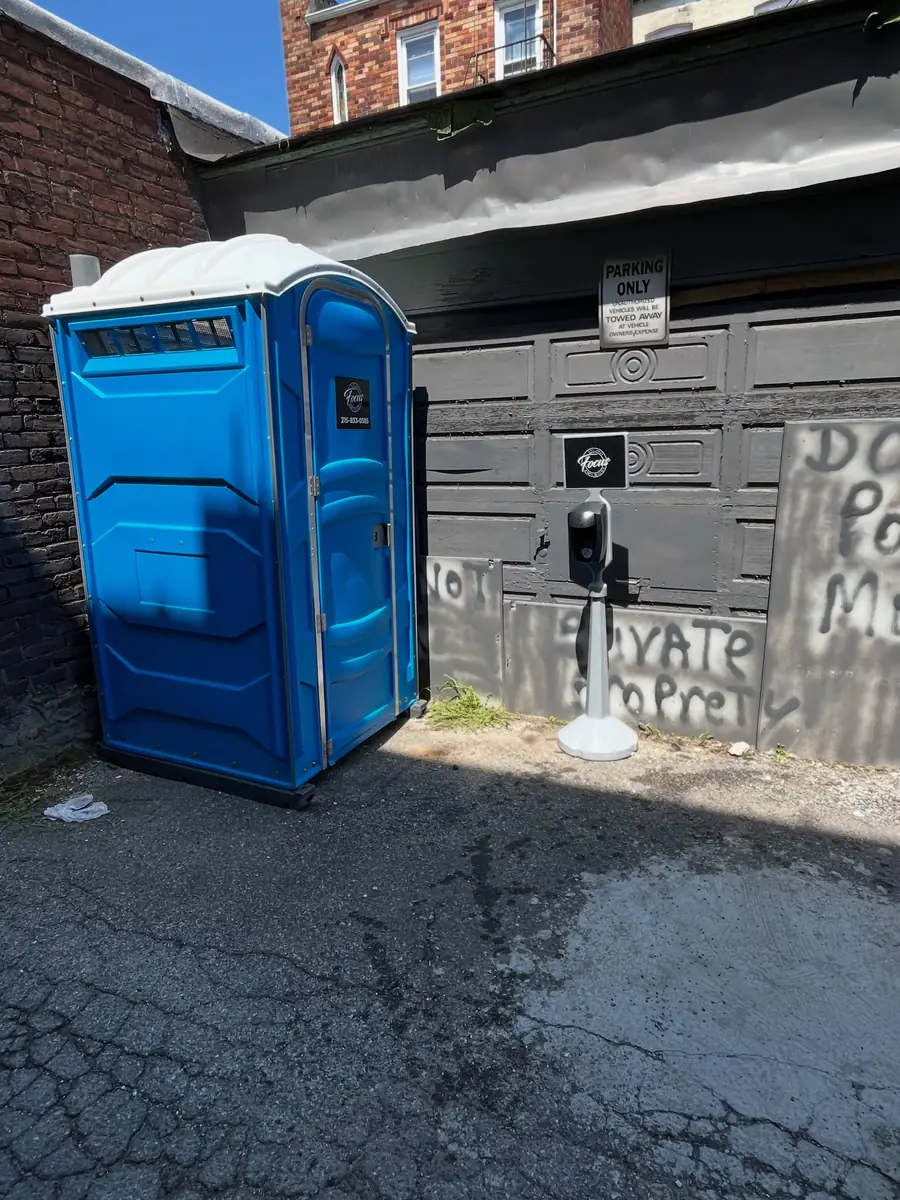 Blue porta potty placed off the pavement beside a garage