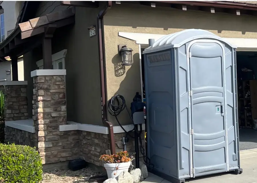 Gray porta potty set on a driveway beside a house remodel