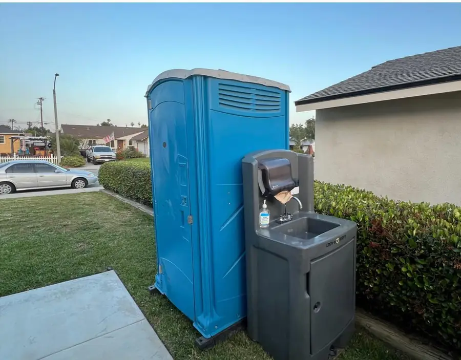 Blue porta potty with a handwashing station beside a home